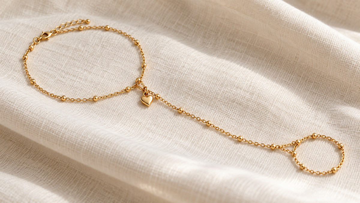 Gold tone hand chain connecting a bracelet and ring with a small heart charm