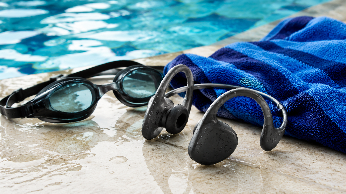 Generic waterproof headphones beside swimming goggles and a pool towel