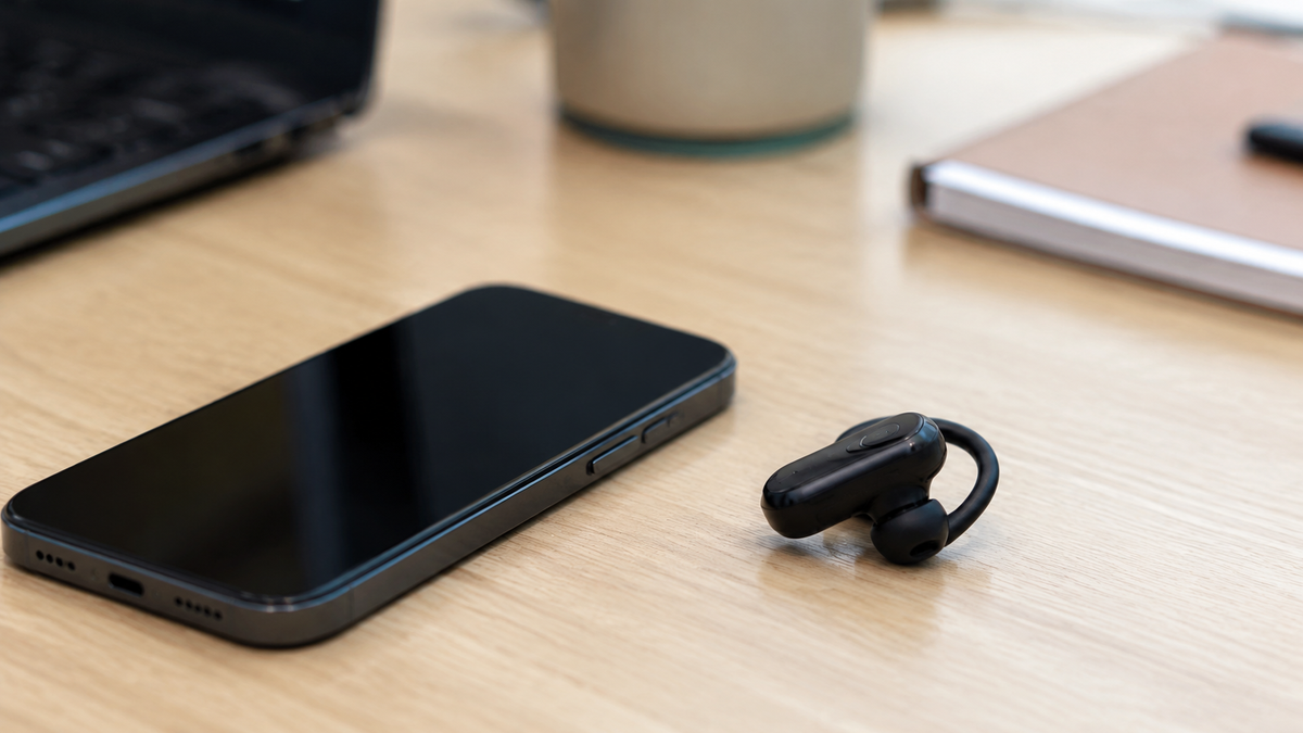 Compact single-ear wireless earpiece beside a phone
