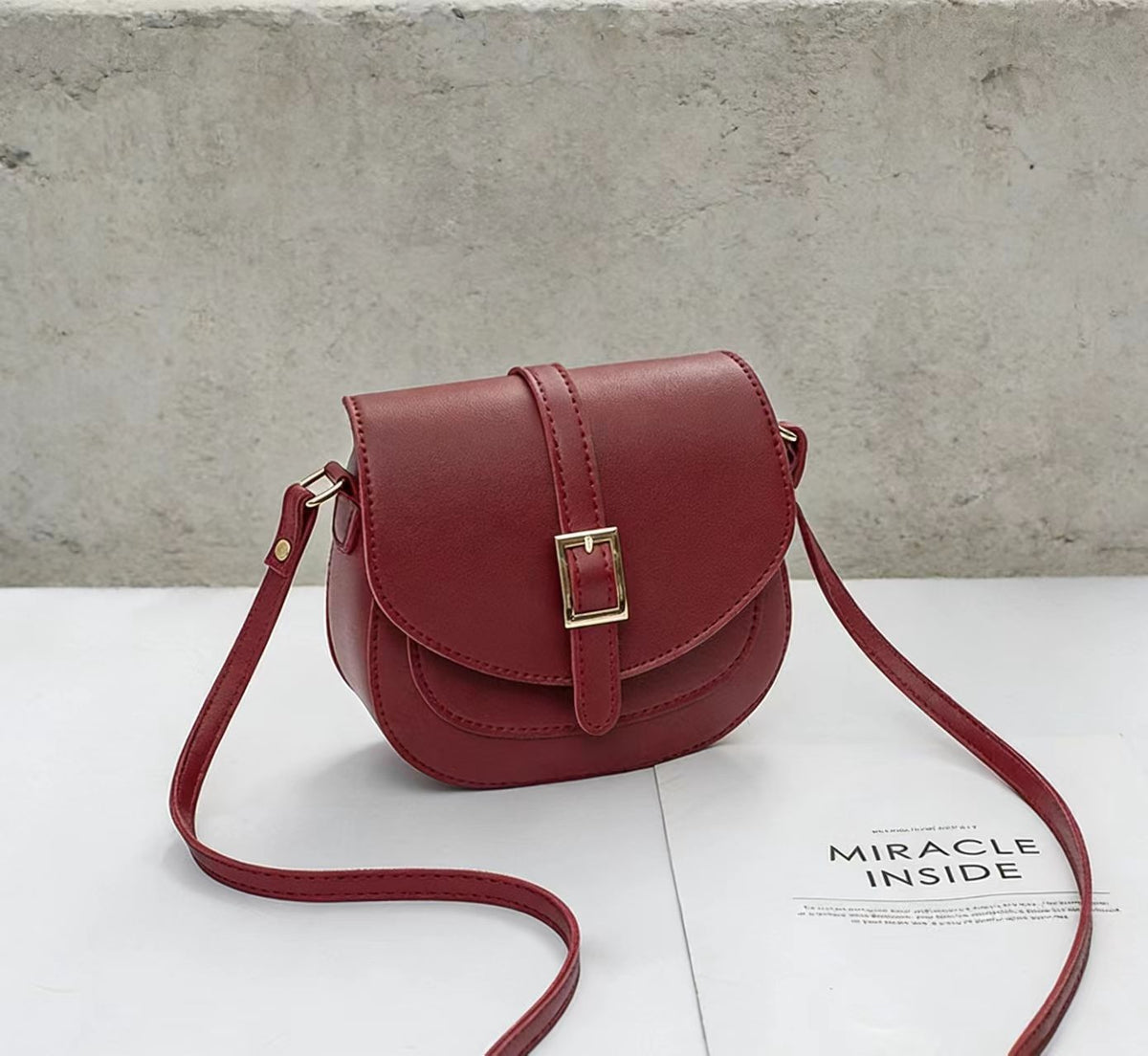 Simple metal-buckle flap crossbody saddle bag with an adjustable shoulder strap.
